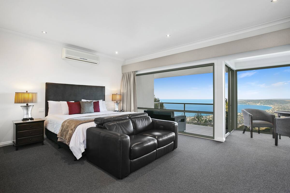 Una habitación de hotel moderna con una cama grande, un sofá de cuero, un escritorio y un balcón con vistas al mar.