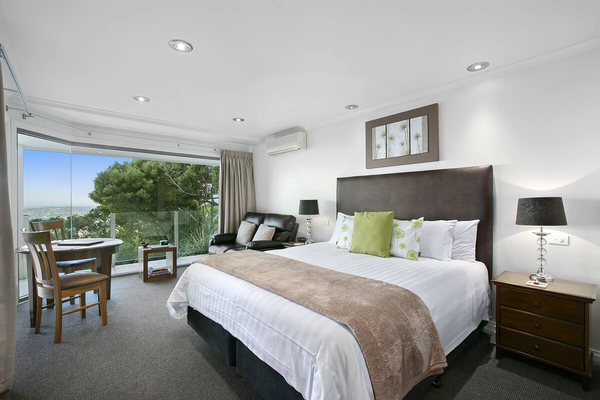 Una habitación de hotel moderna con una cama grande, un escritorio y una silla. Se ve el exterior a través de la ventana.