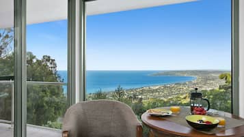 Un comedor con una mesa dispuesta para el desayuno, una silla y vistas al mar y al pueblo.