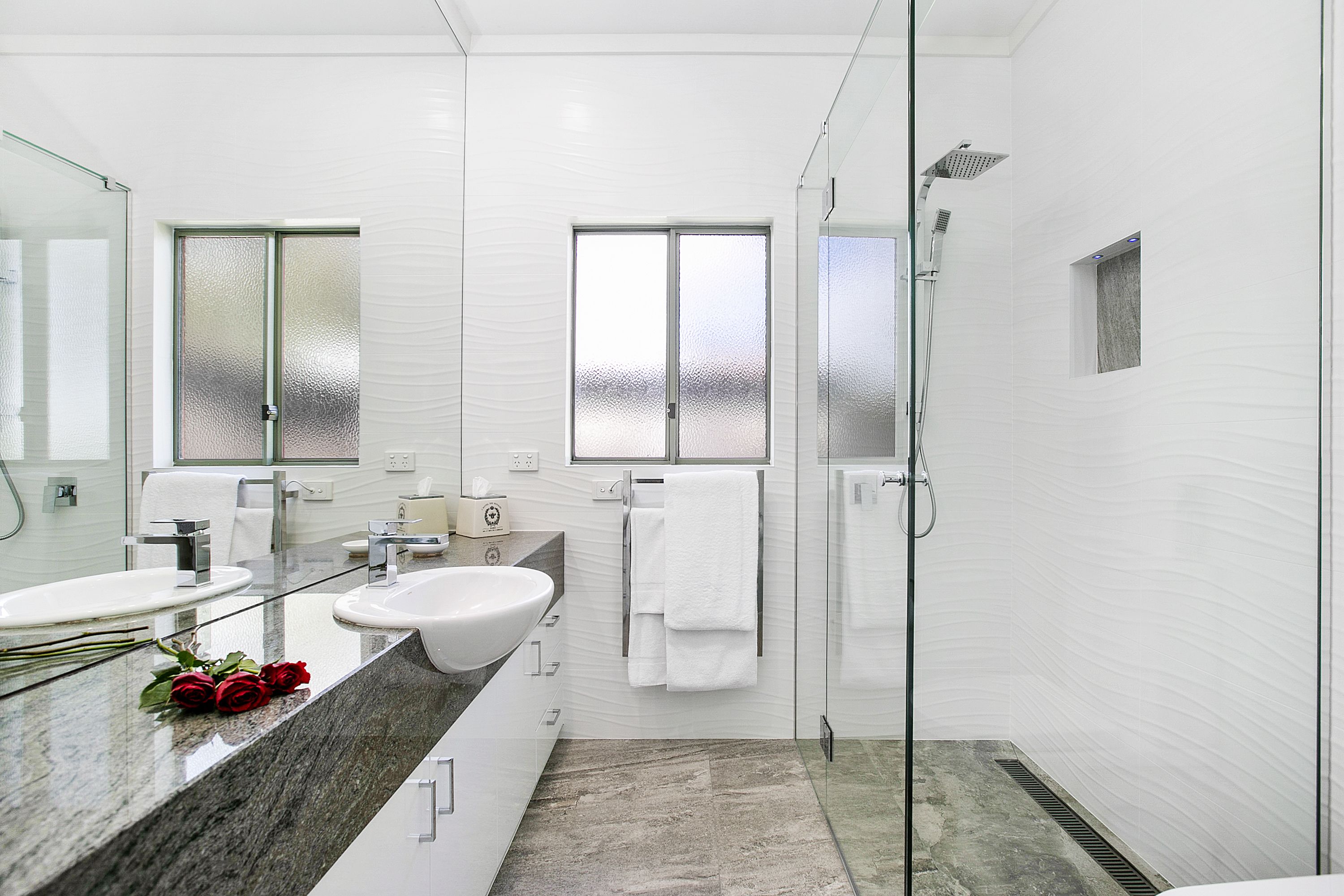 A modern bathroom with two sinks, a glass shower enclosure, and a large mirror.
