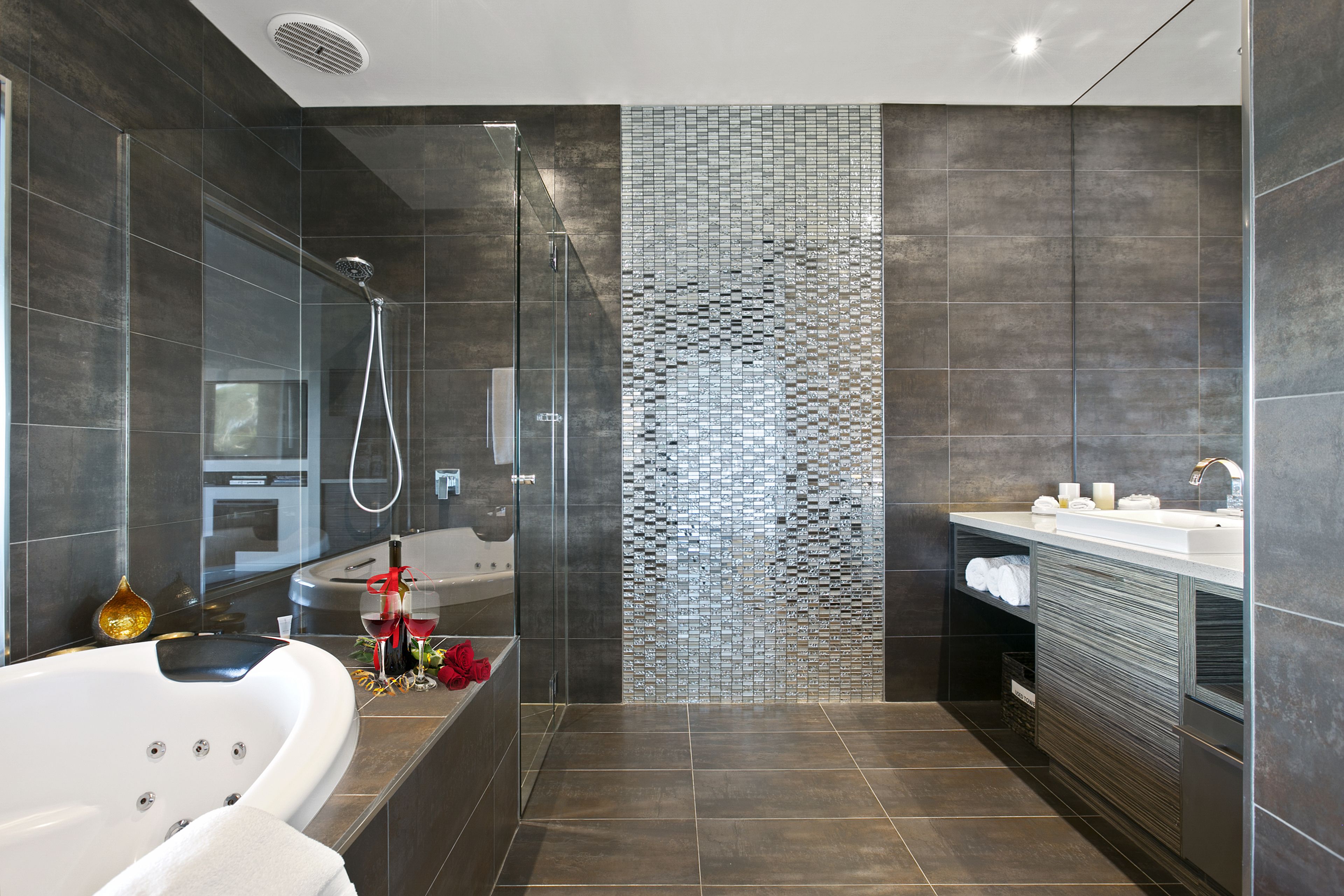 A modern bathroom with a glass-enclosed shower, a freestanding bathtub, and a tiled wall with a unique pattern.