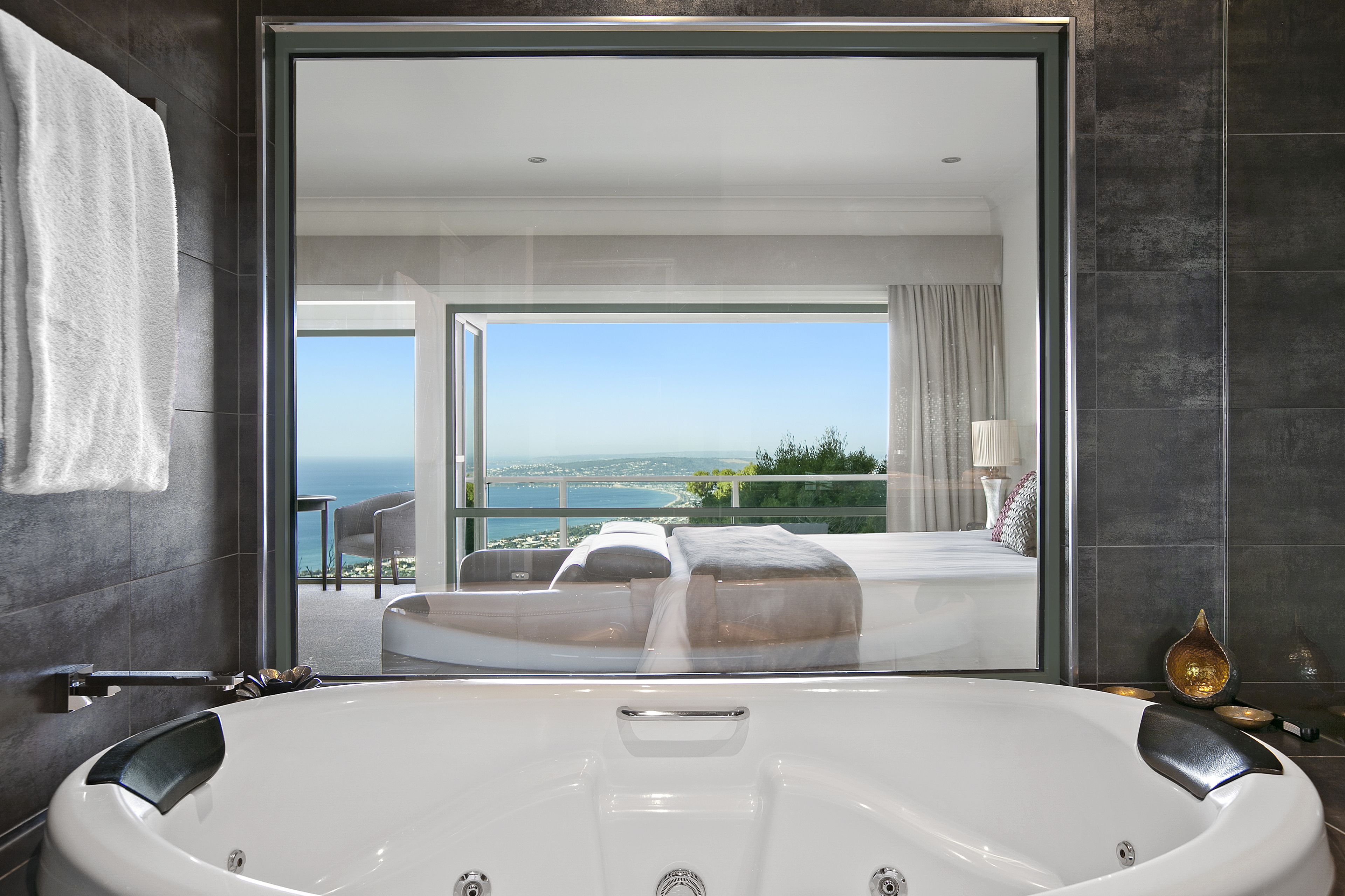 Une salle de bain moderne dotée d’une grande baignoire, d’une douche en verre et offrant une vue sur une chambre avec un lit et un balcon donnant sur la mer.