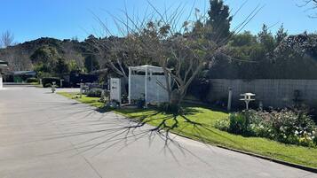 Un sendero pavimentado que conduce a un área de descanso cubierta, con una cerca blanca y plantas en macetas.