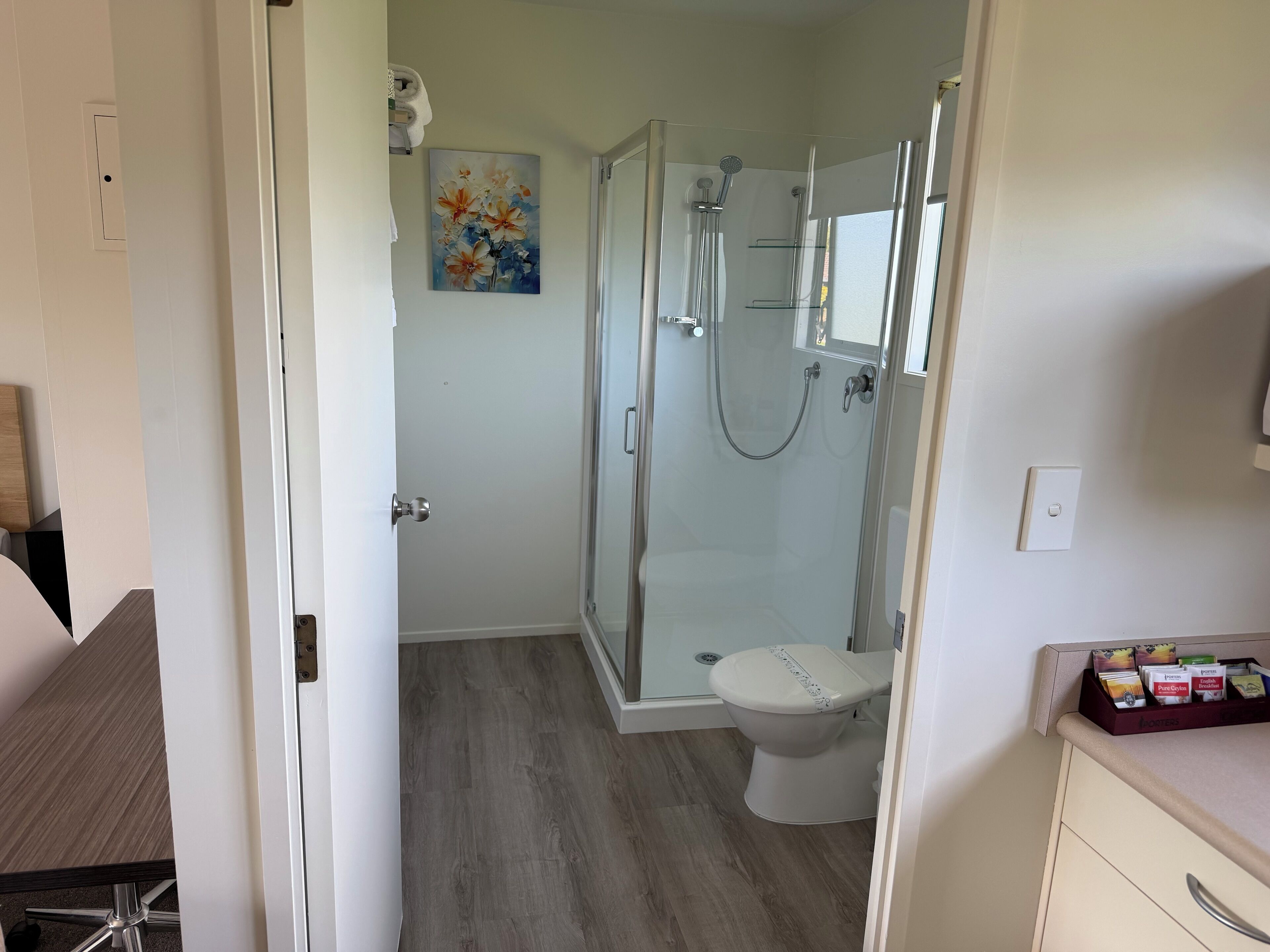 Ein modernes Badezimmer mit einer gläsernen Duschkabine, einer Toilette und Holzboden.