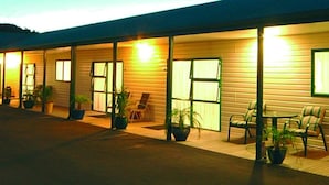A motel with multiple rooms, each with a window and a door. There are several potted plants and outdoor seating areas with chairs. - Coromandel Court Motel (Coromandel)