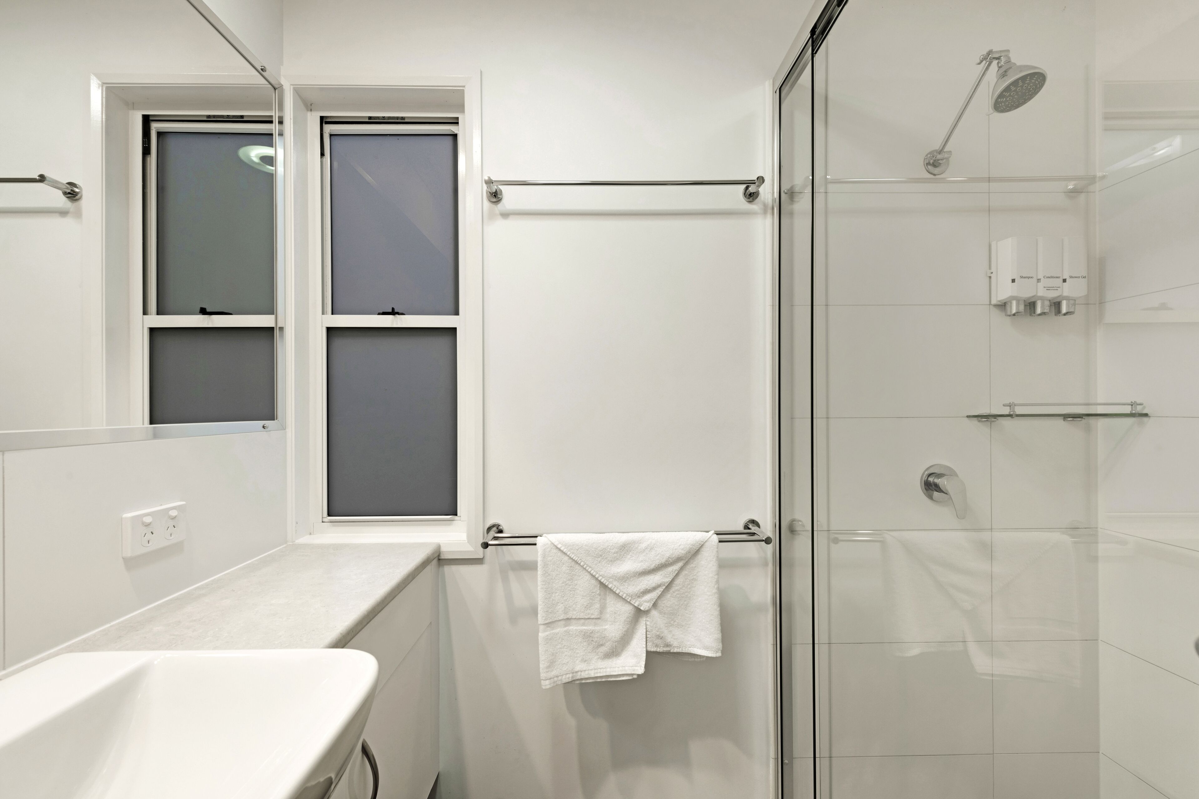 A modern bathroom with a glass shower enclosure, a white sink, and a towel rack.