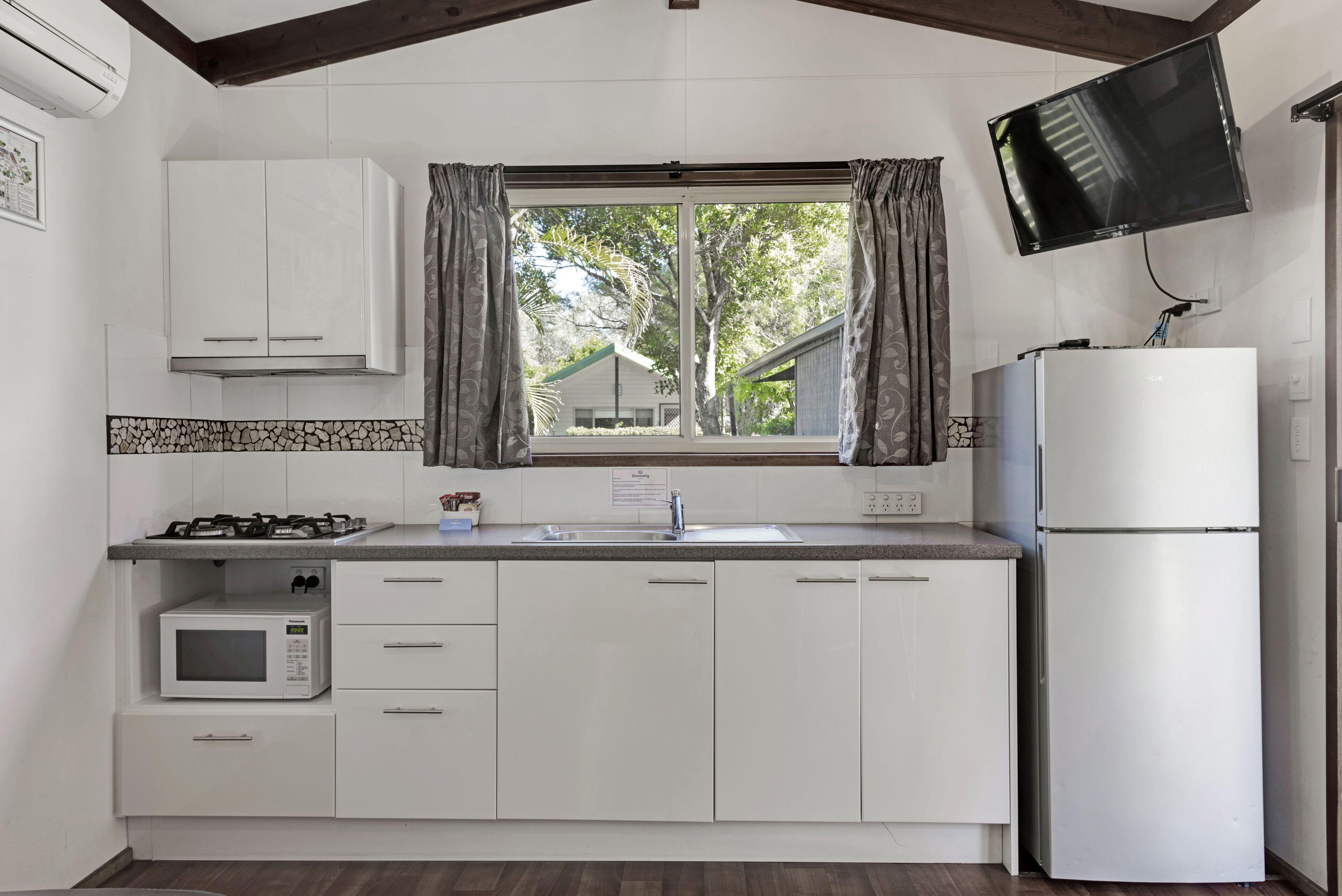 Une cuisine avec des meubles blancs, un four à micro-ondes, une cuisinière à gaz, un évier et un réfrigérateur.
