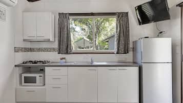 Una cocina con armarios blancos, microondas, estufa a gas, lavaplatos y refrigerador.