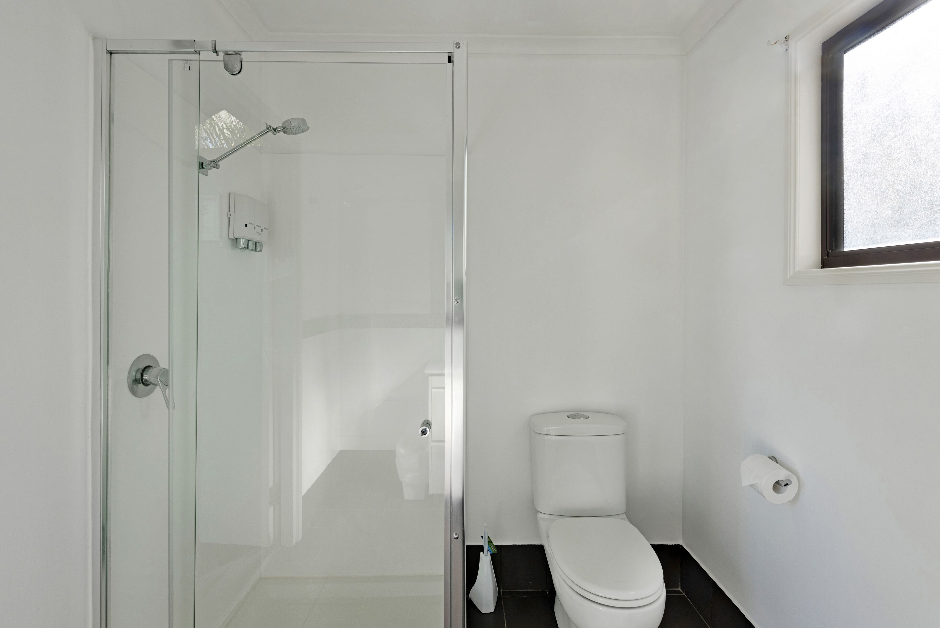 A bathroom with a glass shower enclosure, a toilet, and a window.