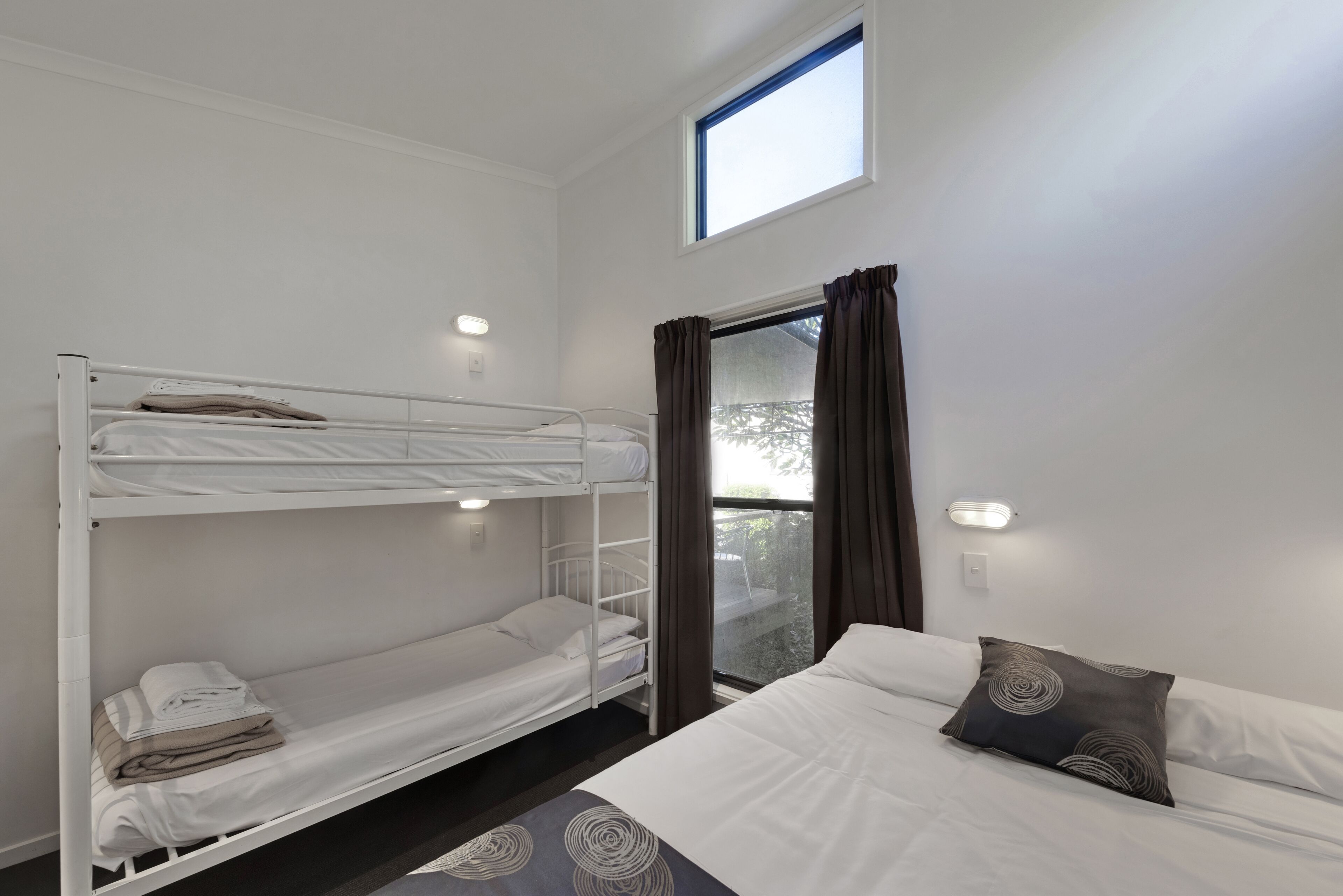 Une chambre avec un lit superposé, une fenêtre et un lit simple.