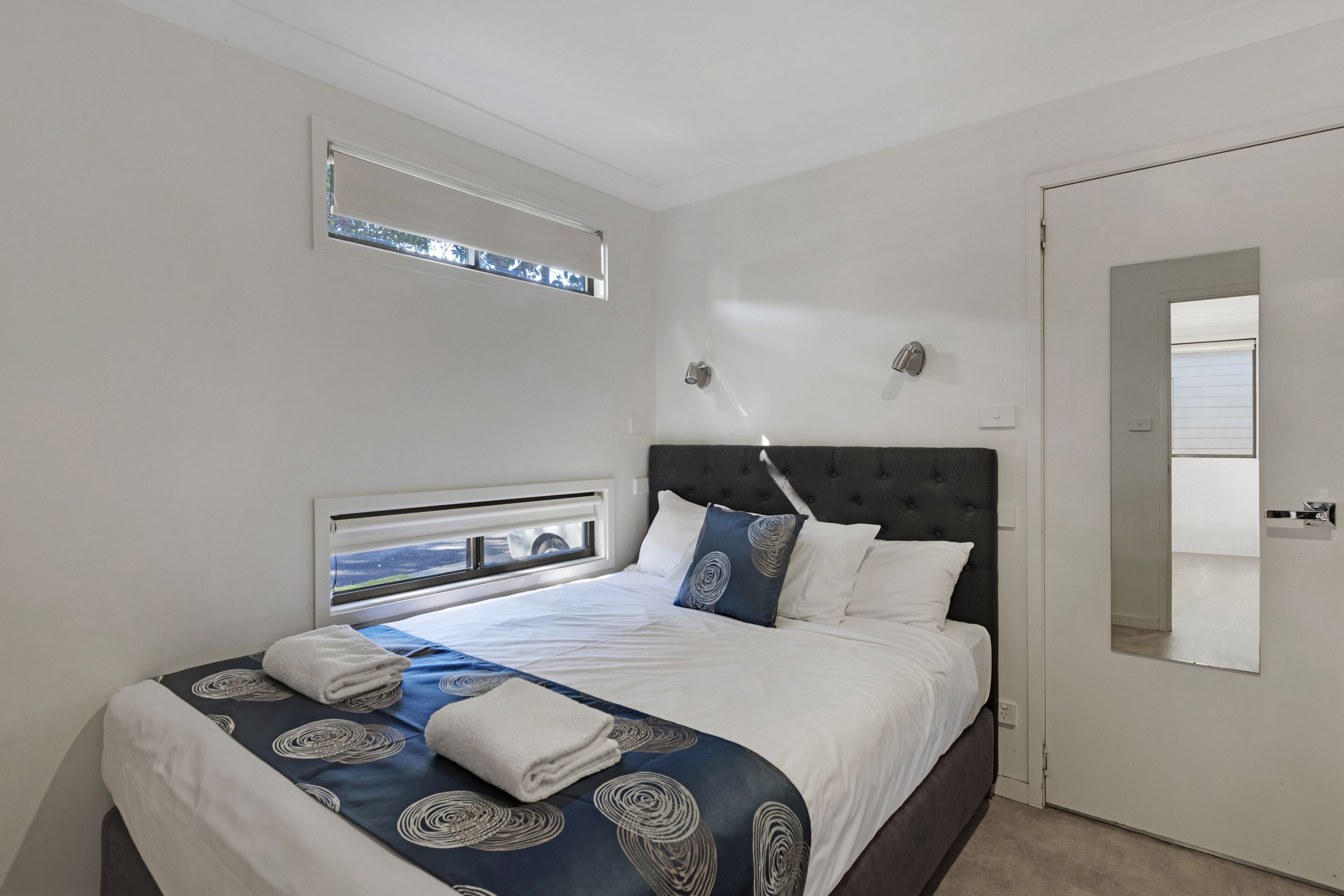 Een slaapkamer met een bed, een raam, een deur en een spiegel.