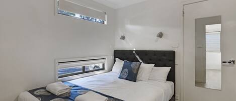 Een slaapkamer met een bed, een raam, een deur en een spiegel.