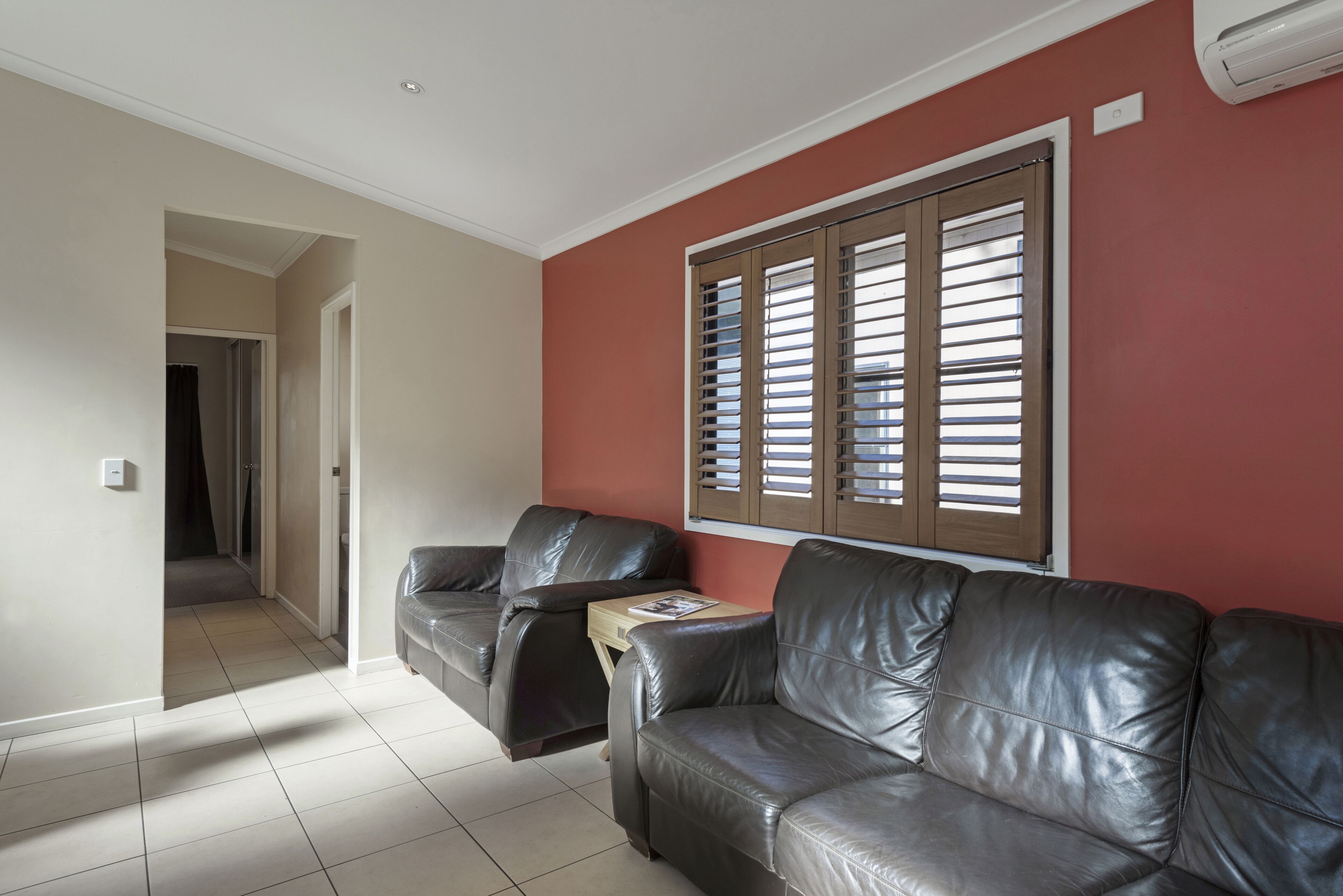 A room with two leather sofas, a small wooden side table, and a window with blinds.