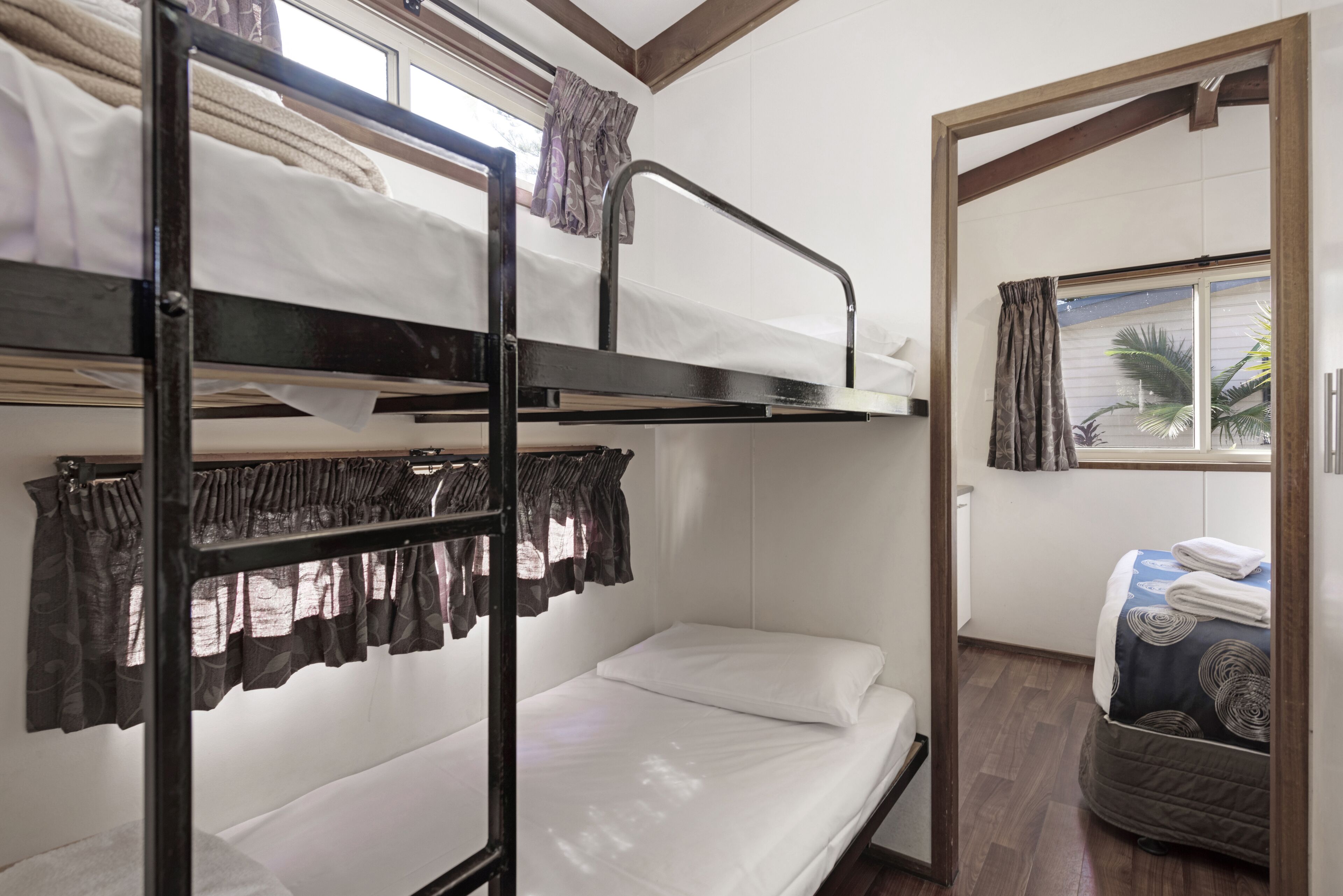 Une chambre avec un lit superposé, une fenêtre, des rideaux et une porte donnant sur une autre pièce.