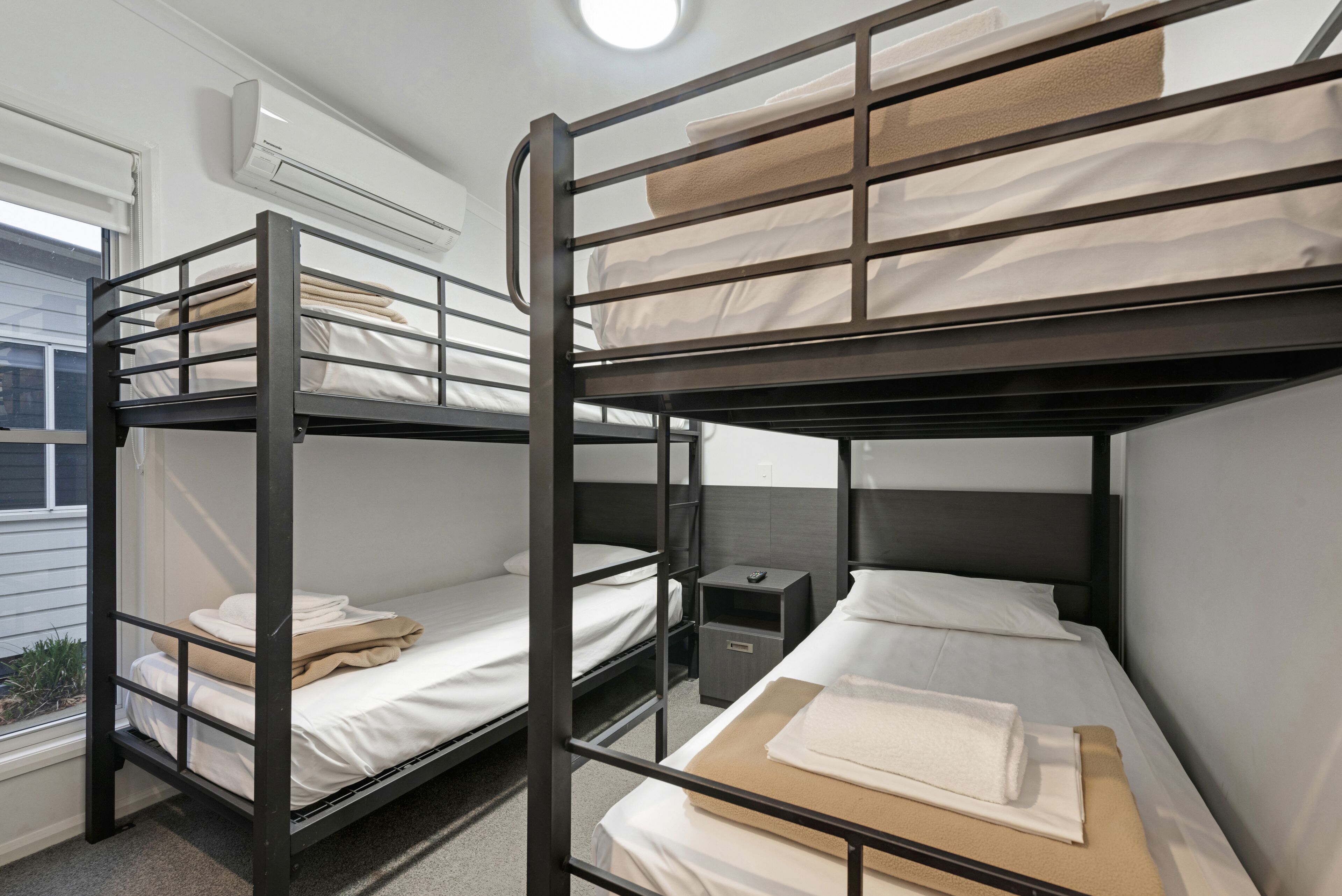 Un dormitorio con literas, una mesita de noche pequeña y una ventana con persianas.