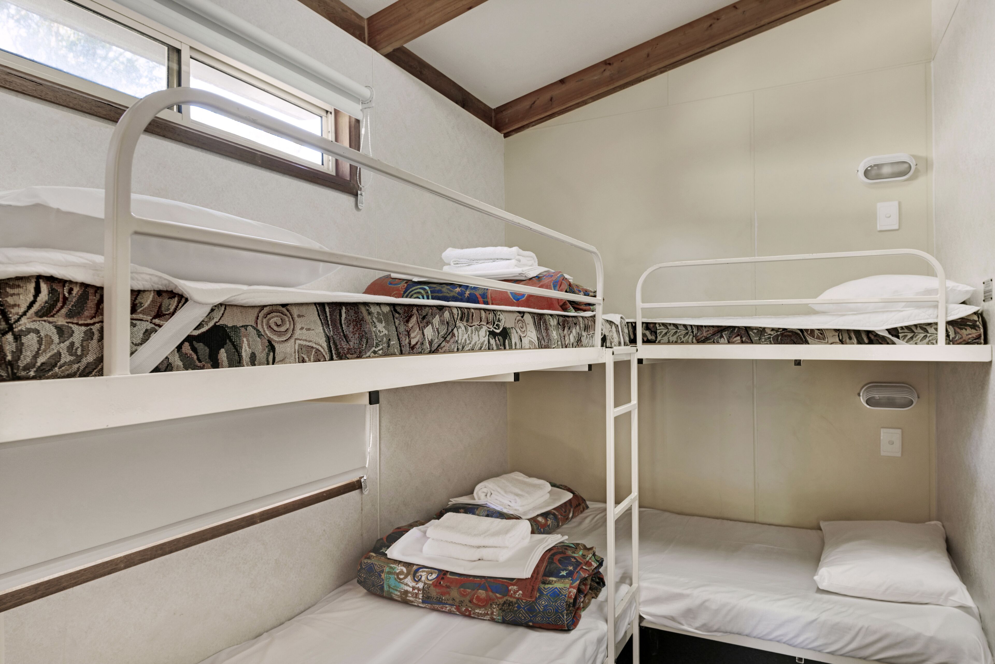 A bunk bed room with a window, a small table, and a wall-mounted light fixture.