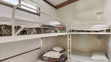 A bunk bed room with a window, a small table, and a wall-mounted light fixture.
