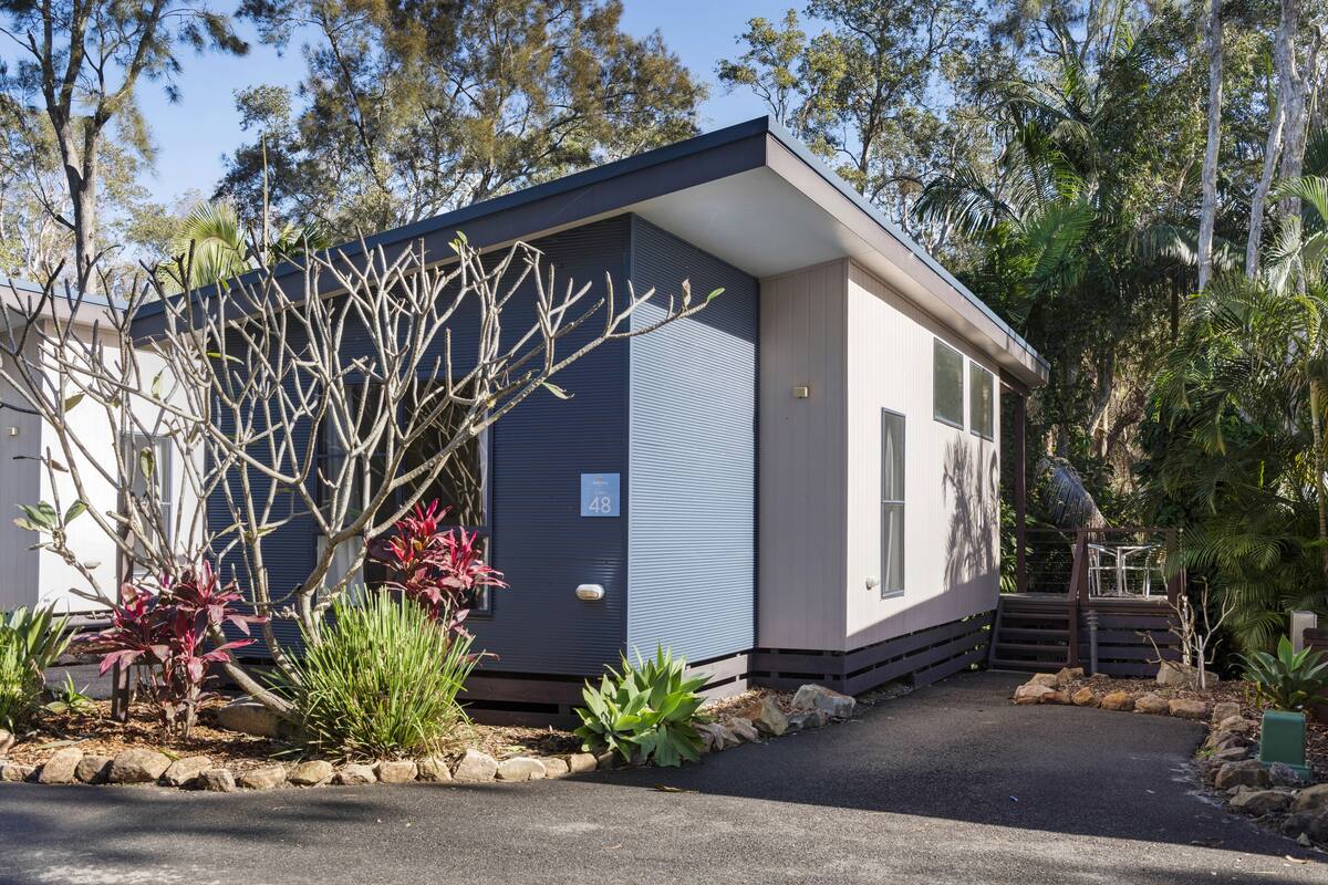 Una casa moderna de dos pisos con fachada azul, rodeada por un jardín ajardinado con diversas plantas y un camino de acceso pavimentado.