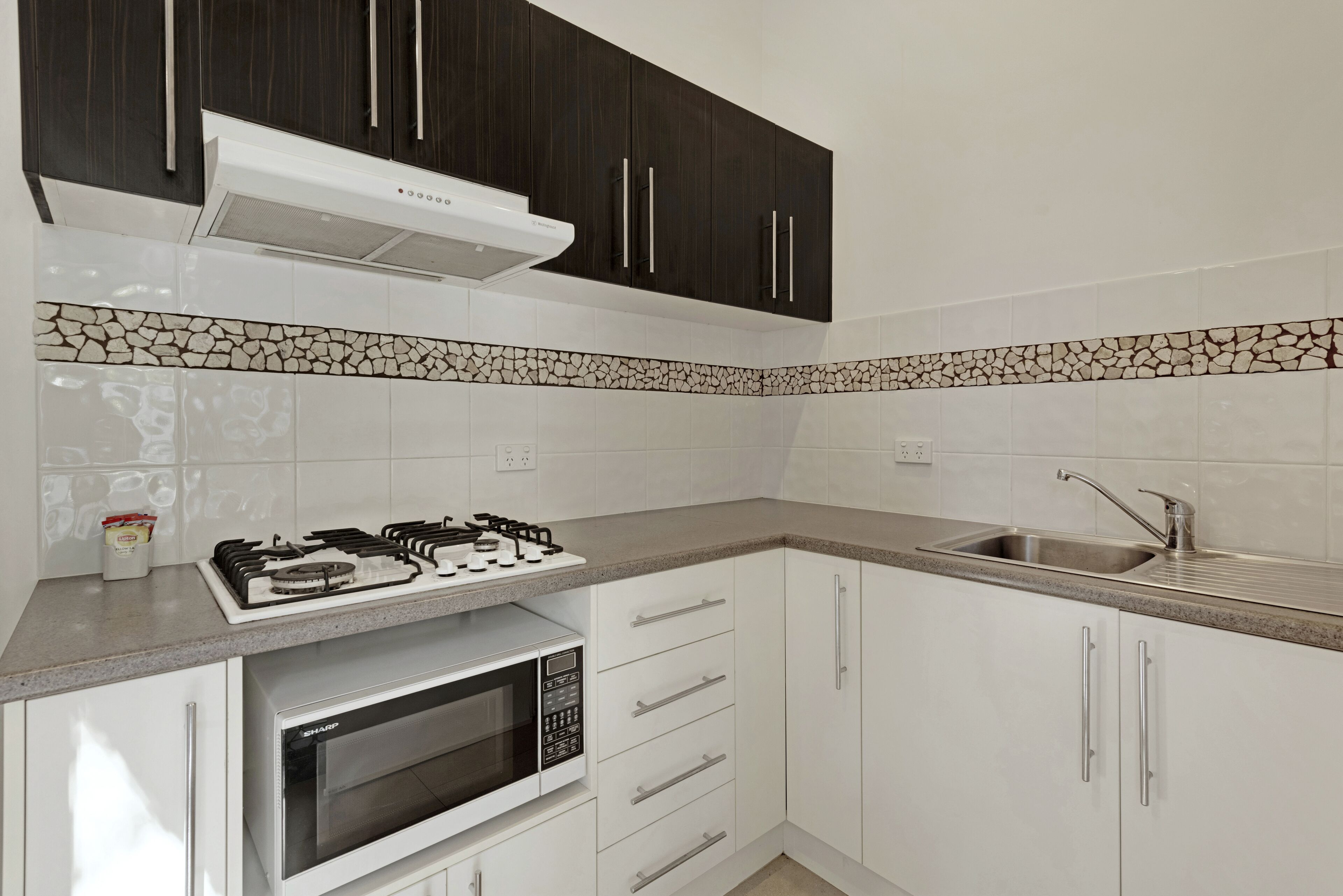 A modern kitchen with dark cabinets, white countertops, a gas stove, a microwave, and a sink.