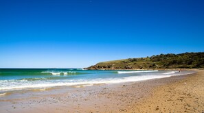 A beach with clear blue water, a sandy shore, and a hilly landscape in the background. - Discovery Parks - Emerald Beach (Emerald Beach)