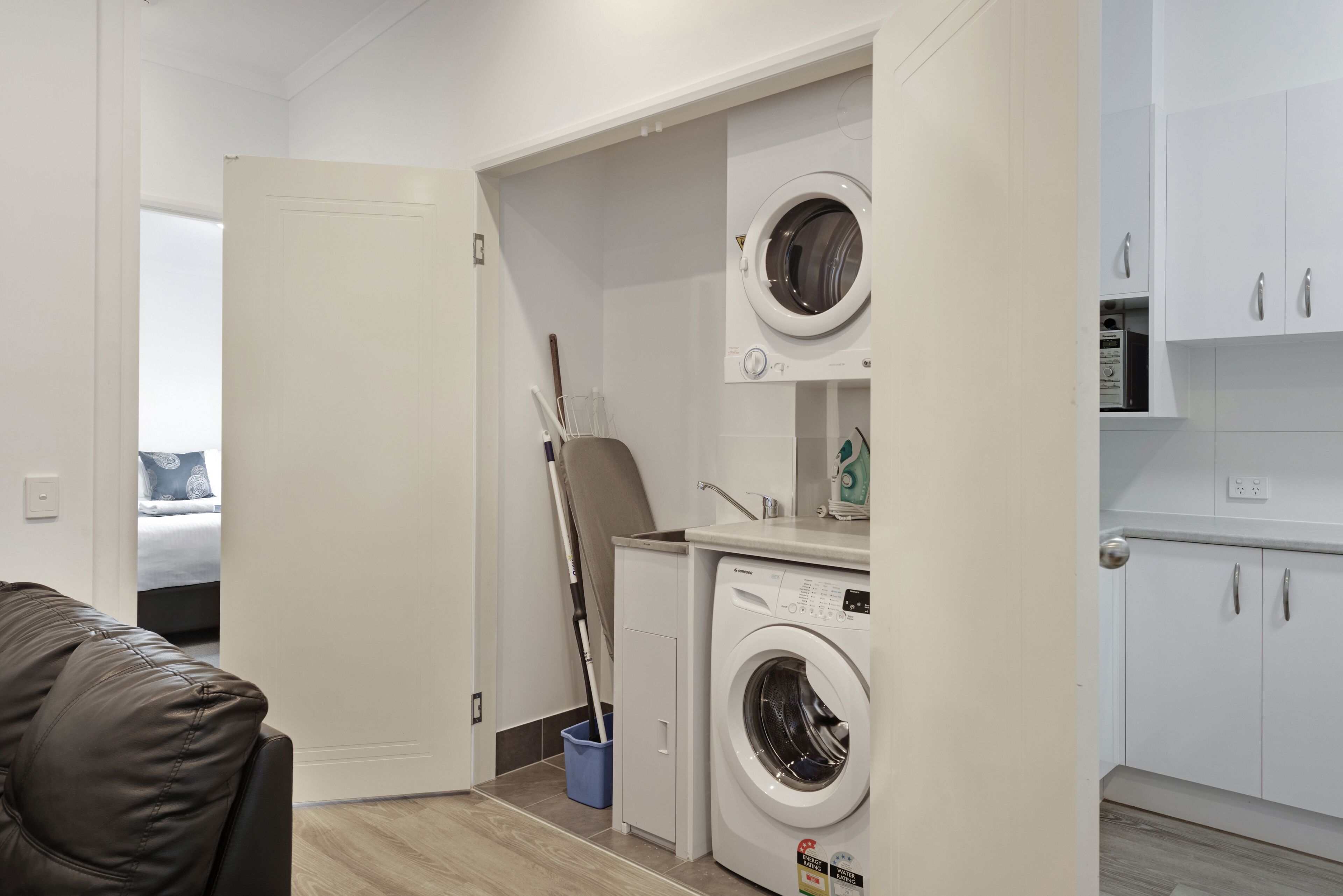 A compact laundry room with a washing machine, a drying rack, and a broom.