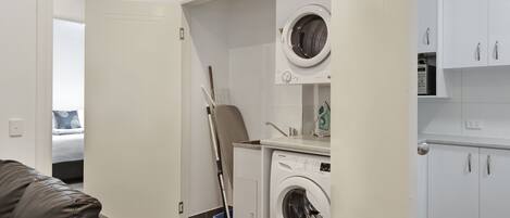 A compact laundry room with a washing machine, a drying rack, and a broom.