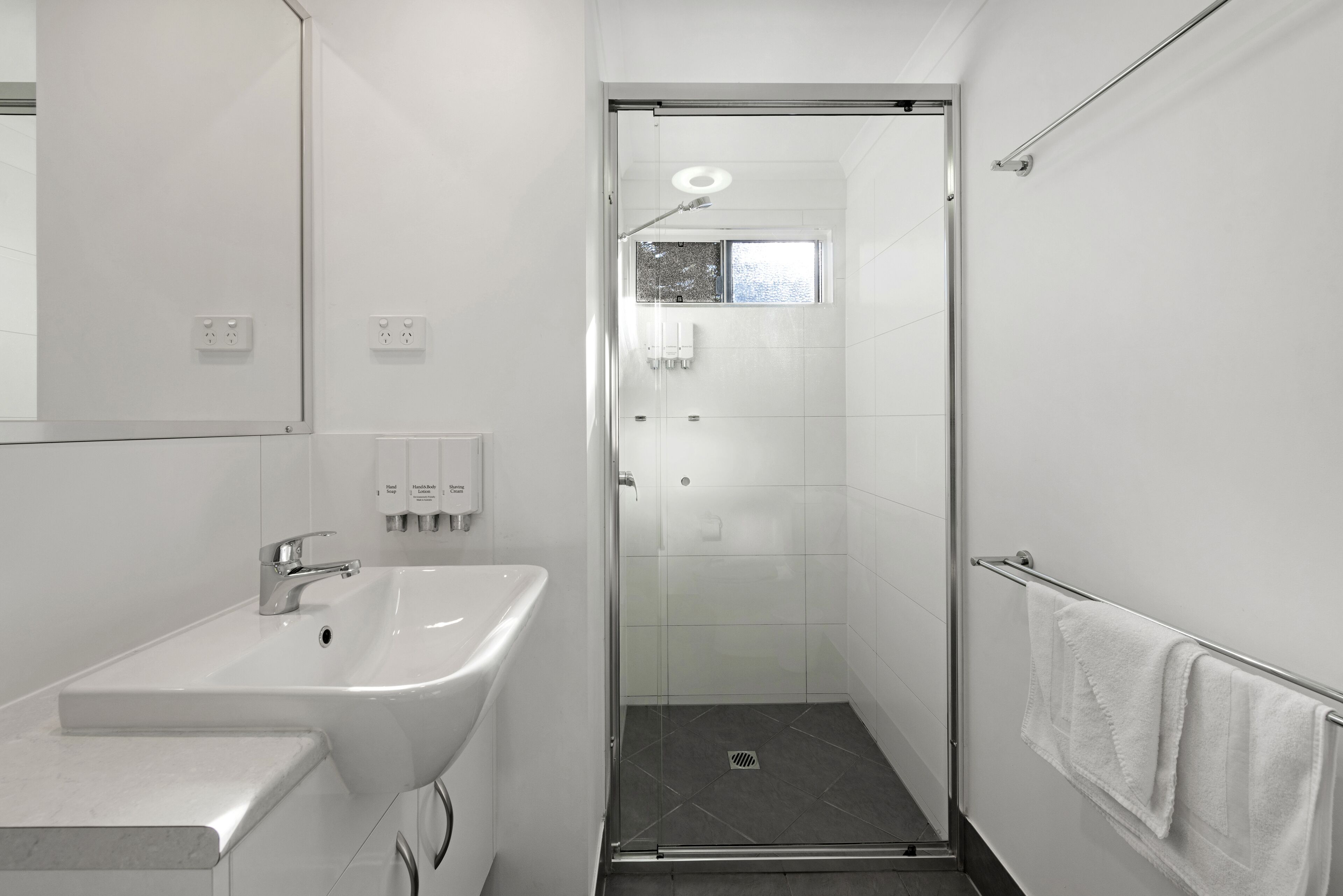 Ein modernes Badezimmer mit Waschbecken in Weiß, einer Glasdusche und einem Handtuchhalter.