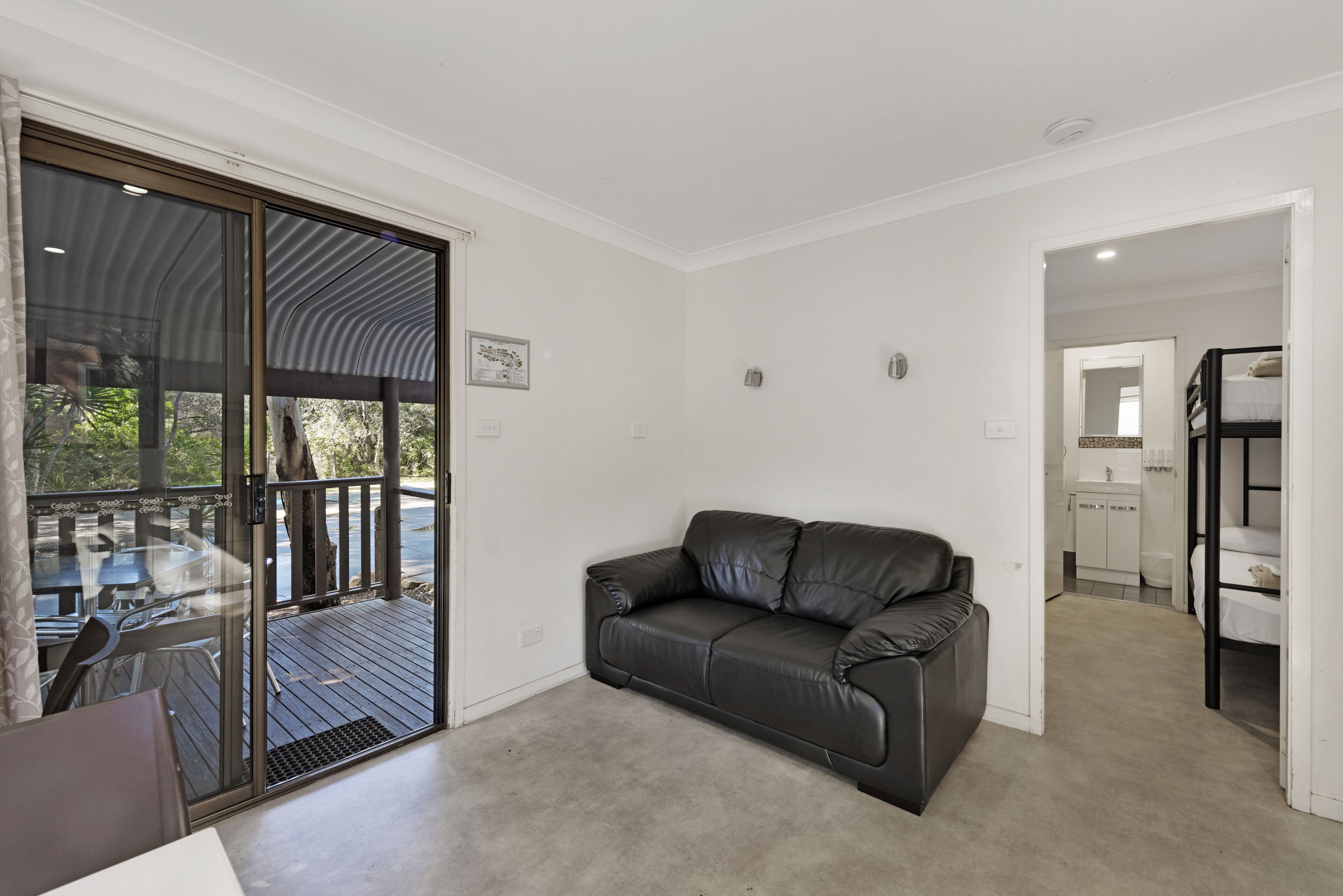 A modern room with a black leather sofa, a glass door leading to an outdoor area, and a kitchenette in the background.