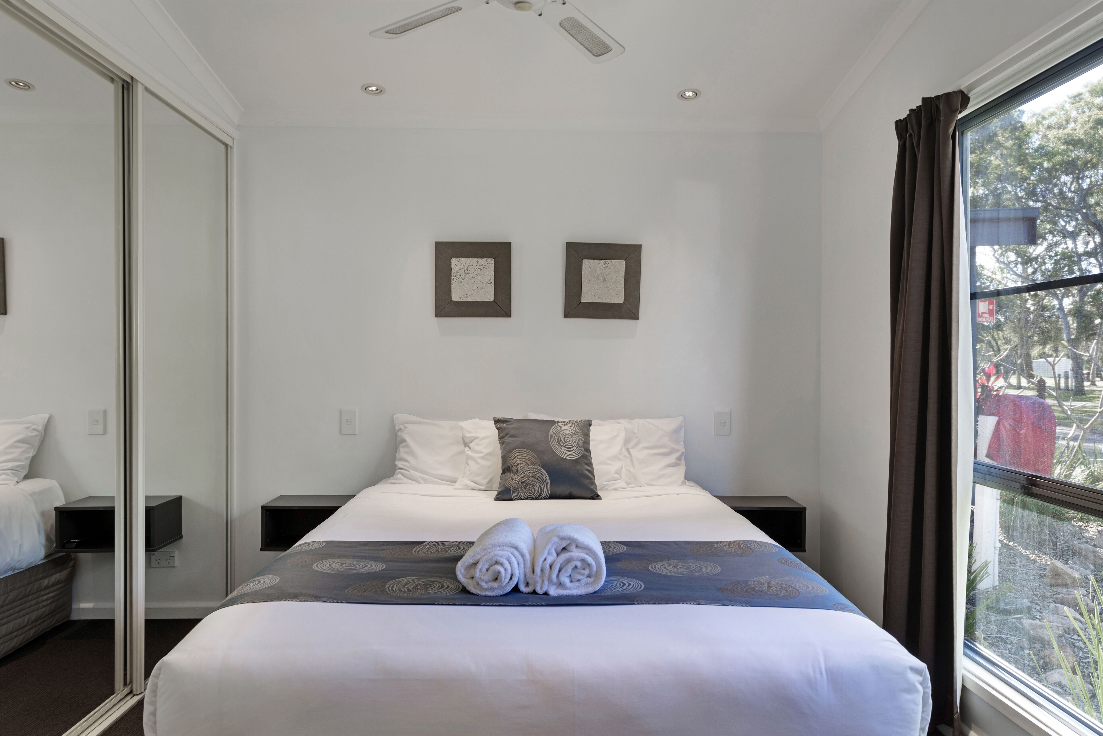 A hotel room with a large bed, two bedside tables, a flat-screen TV, and a window with curtains.