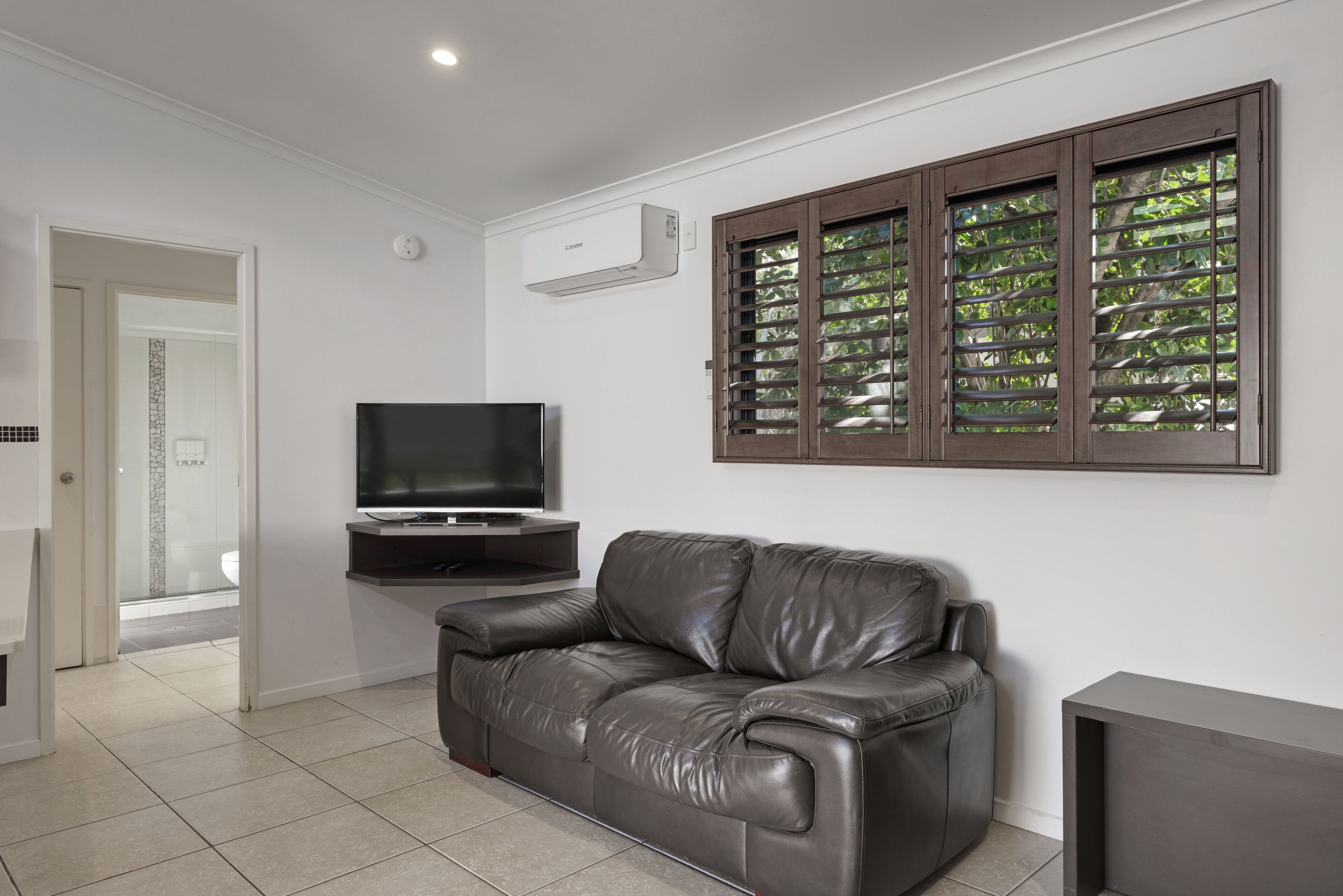 A modern living room with a leather sofa, a flat-screen TV, and a wall-mounted air conditioner.