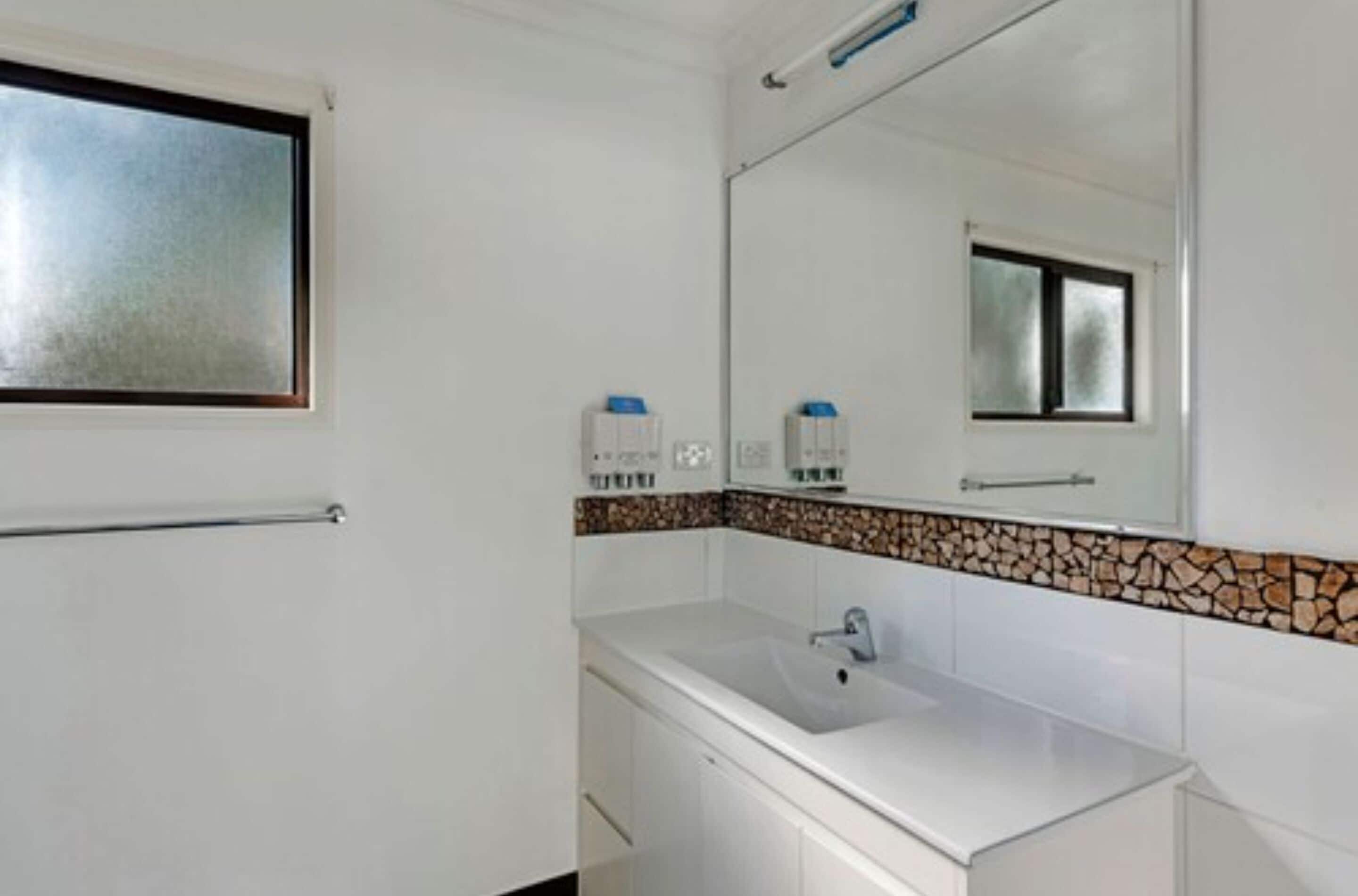 Une salle de bain avec un lavabo blanc, un miroir et une fenêtre.