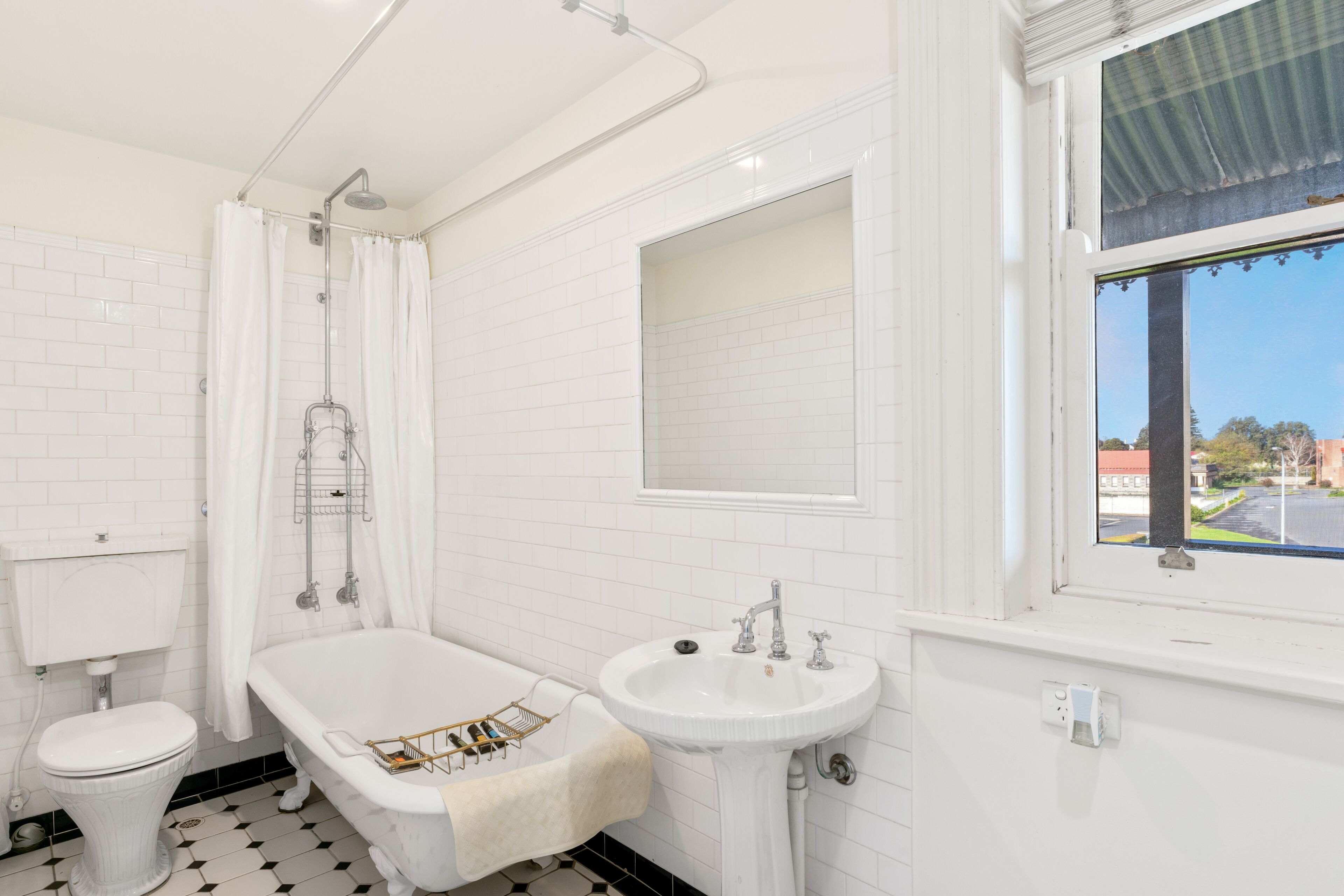 A bathroom with a white bathtub, a sink, and a toilet. There is a window with a view of the outside.