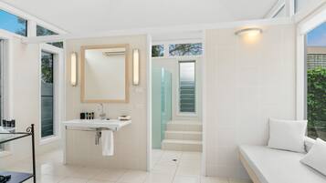 A modern bathroom with a glass shower enclosure, a white sink, and a built-in bench.