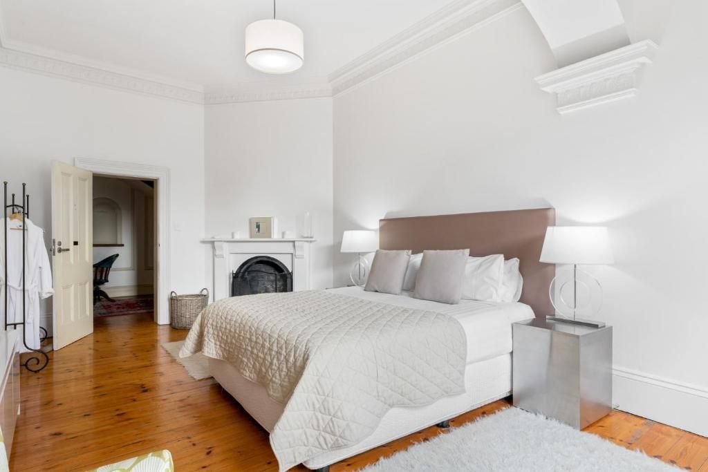 Un dormitorio con una cama grande, lámparas de noche, una chimenea y una puerta blanca que da a otra habitación.