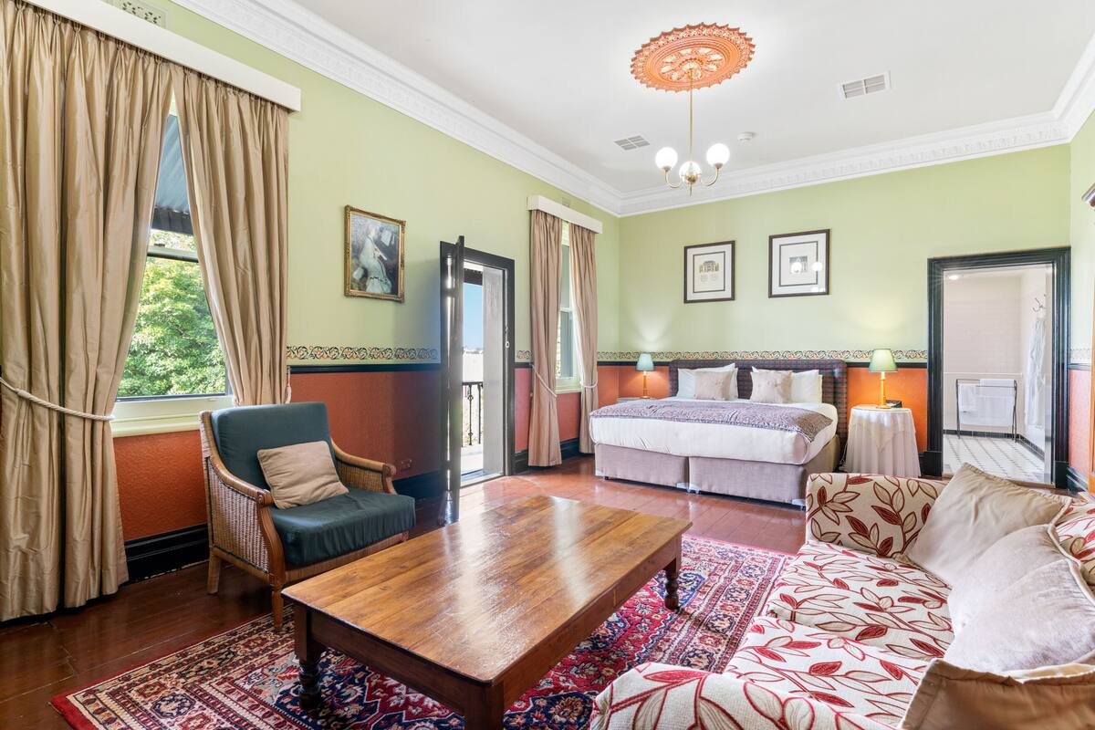 Una habitación con cama, sofá, silla, una mesa de madera y un tapete estampado.