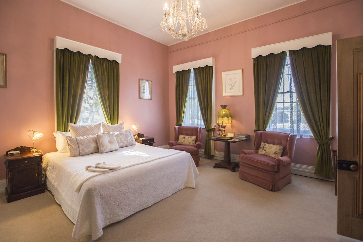 A bedroom with a large bed, two armchairs, a nightstand, and a table with a lamp.