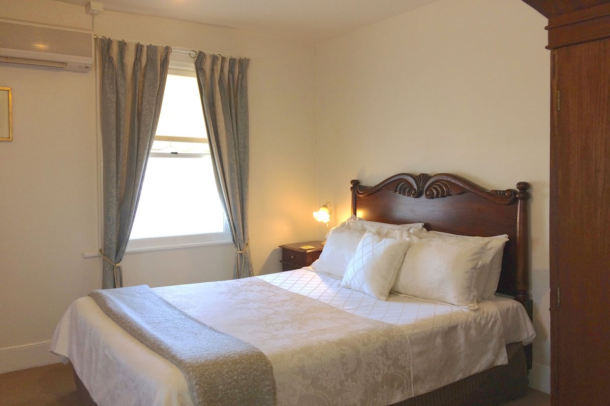 A neatly made bed with a wooden headboard, a bedside lamp, and a window with curtains.
