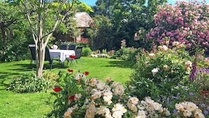 A garden with a dining area, including a table and chairs, surrounded by various flowers and greenery. - The Racecourse Inn (Longford)