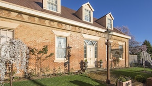 A two-story brick house with a front door, a garage door, and a small garden with flowering plants. - The Racecourse Inn (Longford)
