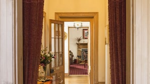 A hallway with a chandelier, wooden door, and a rug leading to a room. - The Racecourse Inn (Longford)