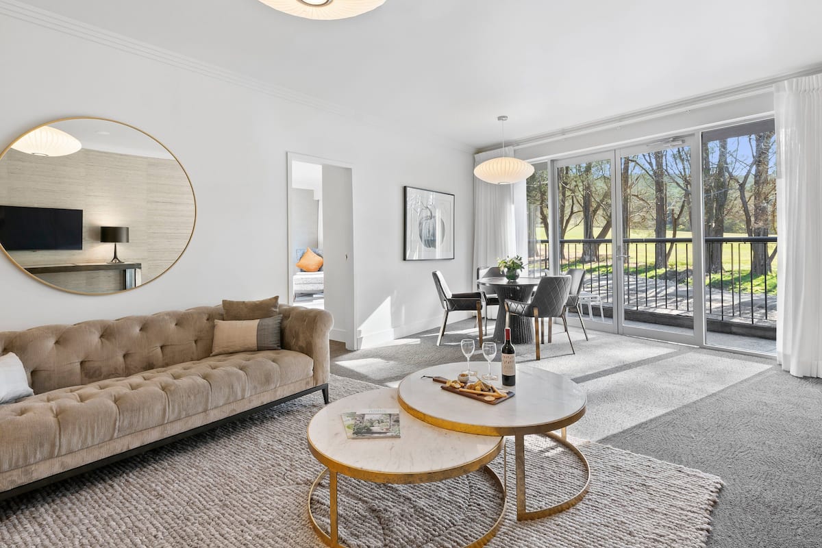 A modern living room with a sofa, a round coffee table, and a dining area with chairs and a table.