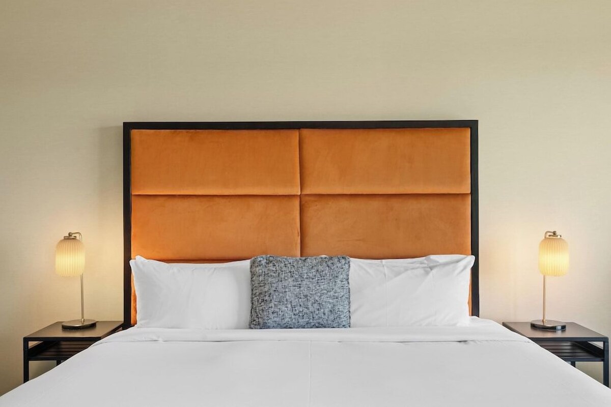 Una habitación de hotel con una cama grande, dos mesitas de noche y un cabecero.