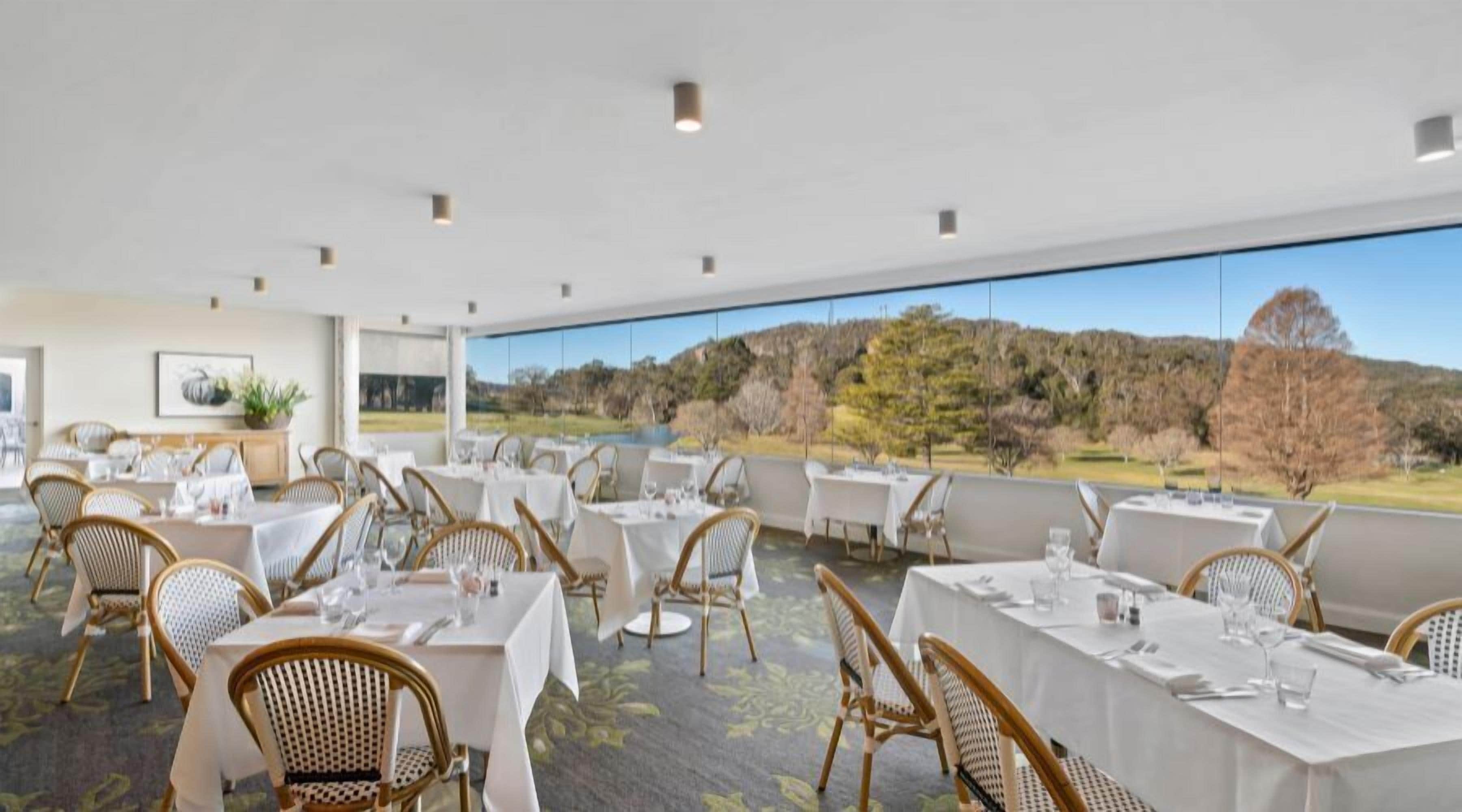 A restaurant with tables set for dining, featuring a view of a natural landscape.