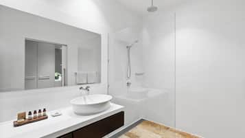 Une salle de bain moderne avec un grand miroir, un lavabo blanc, une douche et un meuble-lavabo sur lequel est posé un plateau contenant des articles de toilette.
