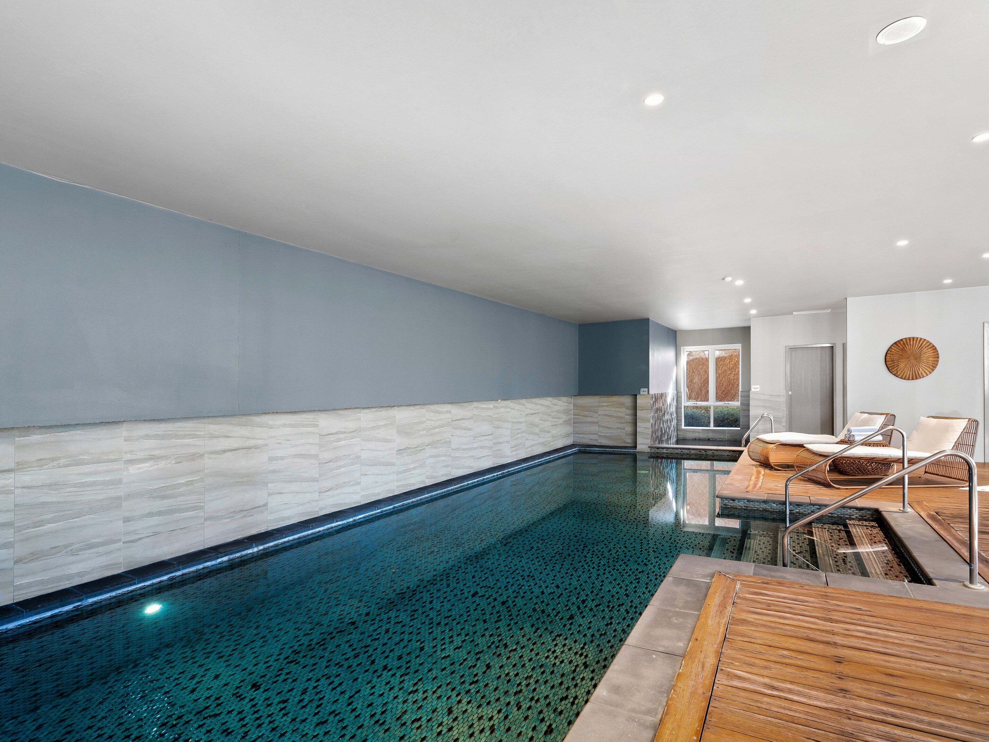A modern indoor swimming pool with clear water, a wooden deck, and lounge chairs.
