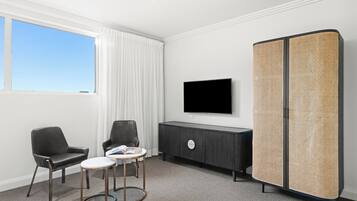 Una habitación de hotel moderna con un ventanal grande, un televisor de pantalla plana, un sofá de cuero negro, una mesita redonda y un separador tejido.