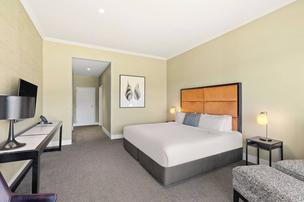 A hotel room with a bed, bedside tables, a desk, and a chair.