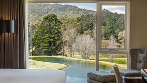 A hotel room with a large window offering a view of a lake and forested hills. - The Gibraltar  (Bowral)