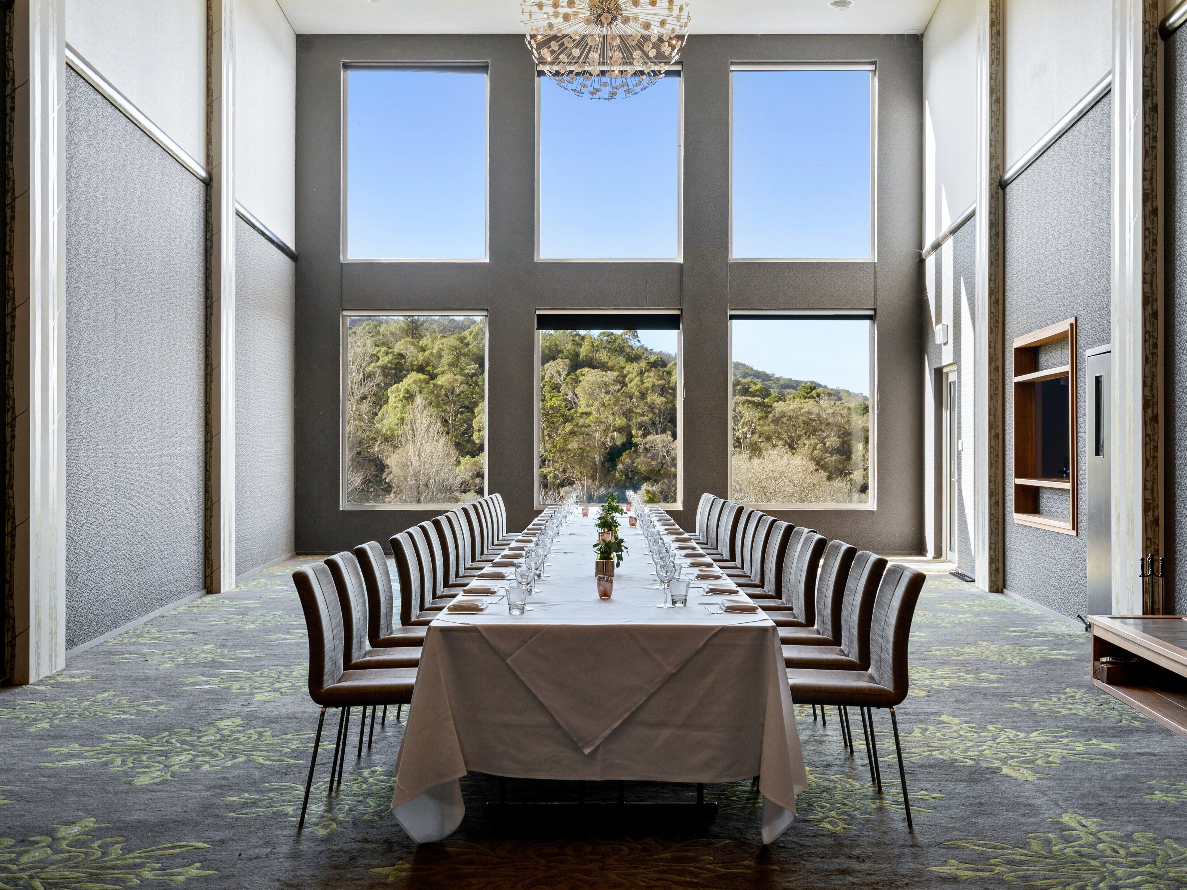 A long dining table with chairs, large windows, and a chandelier.