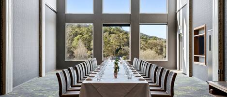A long dining table with chairs, large windows, and a chandelier.